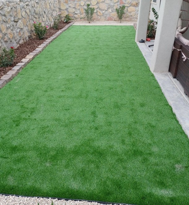 Lush artificial turf lawn installation between stone wall and patio