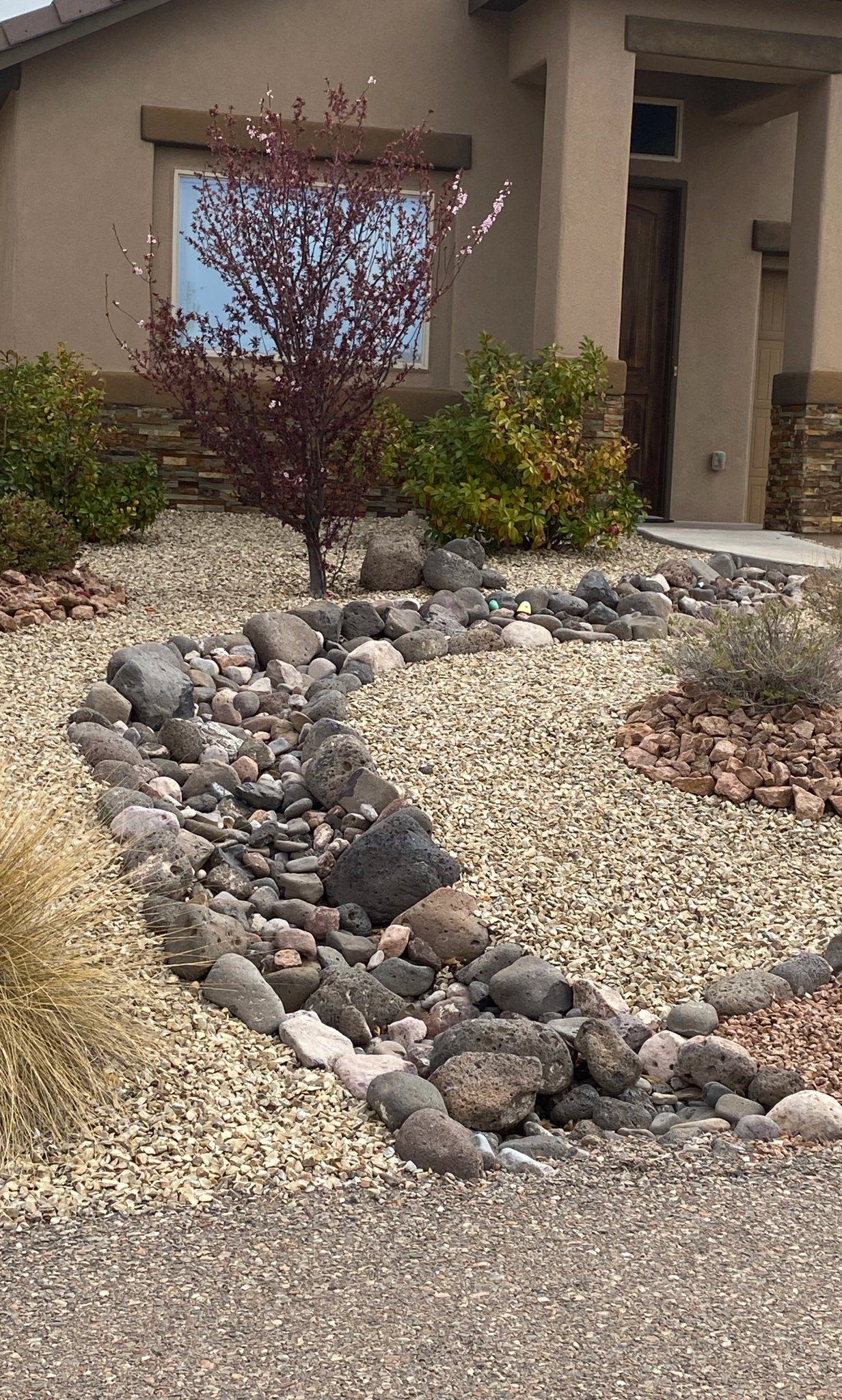 Front-yard French drain disguised as a dry creek bed, preventing standing water at a Las Cruces home by Brainard's Greenscapes